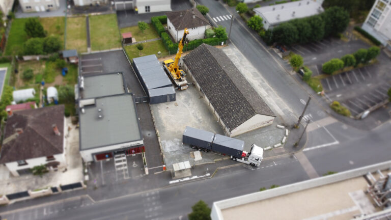 Vue aérienne de huit containers maritimes à Brive-La-Gaillarde pour le parc de selfstockage AUBOX, six sont posées et deux sont encore sur le camion de livraison de VEYNAT, avec la grue de SOMACO en attente du prochain container à poser