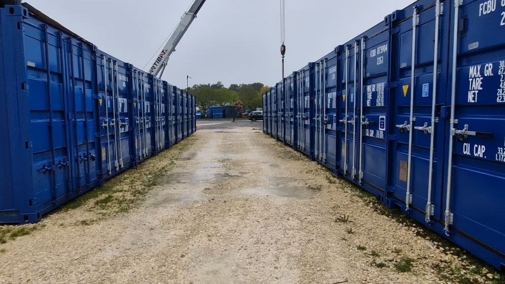 Corridor formé par des rangées de containers de stockage bleus avec une grue au fond chez Selfstock Boulazac.