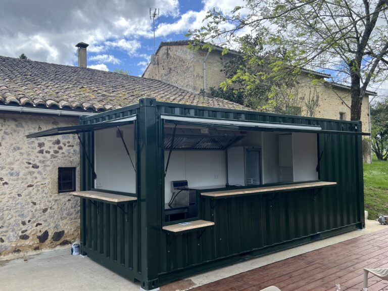 Container snack vert conçu pour la restauration rapide, situé à l'extérieur, devant un bâtiment en pierres anciennes.