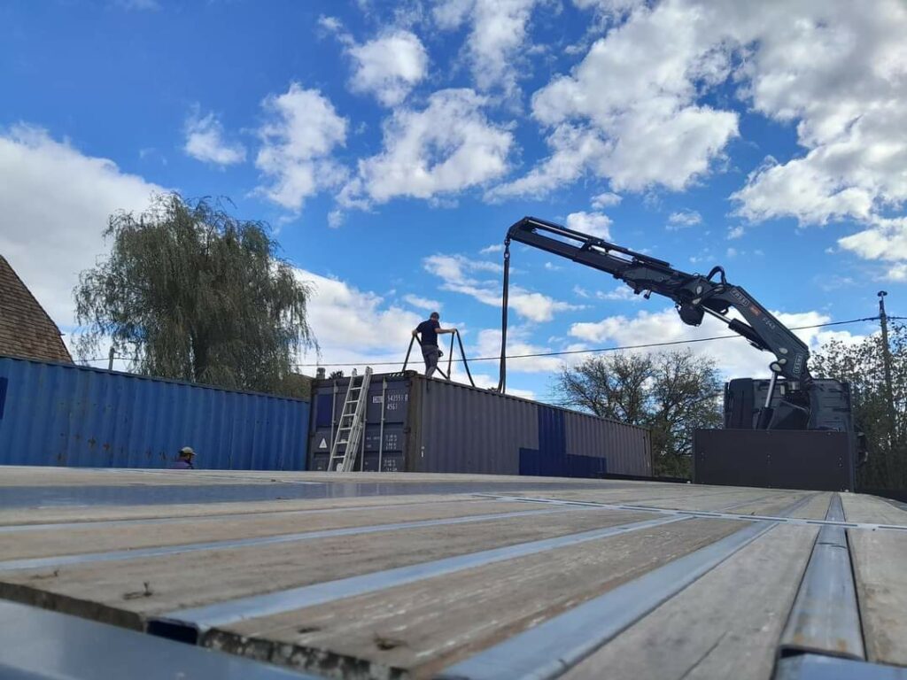 Ouvrier participant à la livraison d'un container maritime bleu pour une maison container dans le Territoire de Belfort, avec grue en arrière-plan.