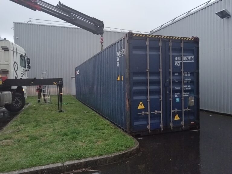 Positionnement précis d'un grand container de stockage 40 pieds bleu par camion grue à côté du bâtiment Intersport Loches.