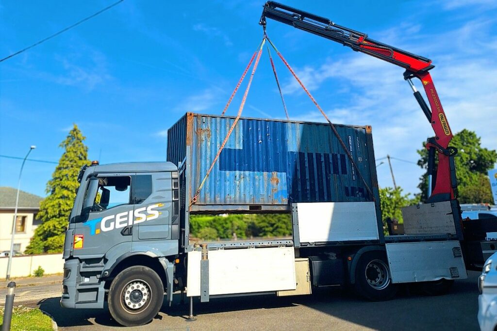 Levage d'un container bleu de 20 pieds par grue de chargement Palfinger à Burnhaupt-le-Haut