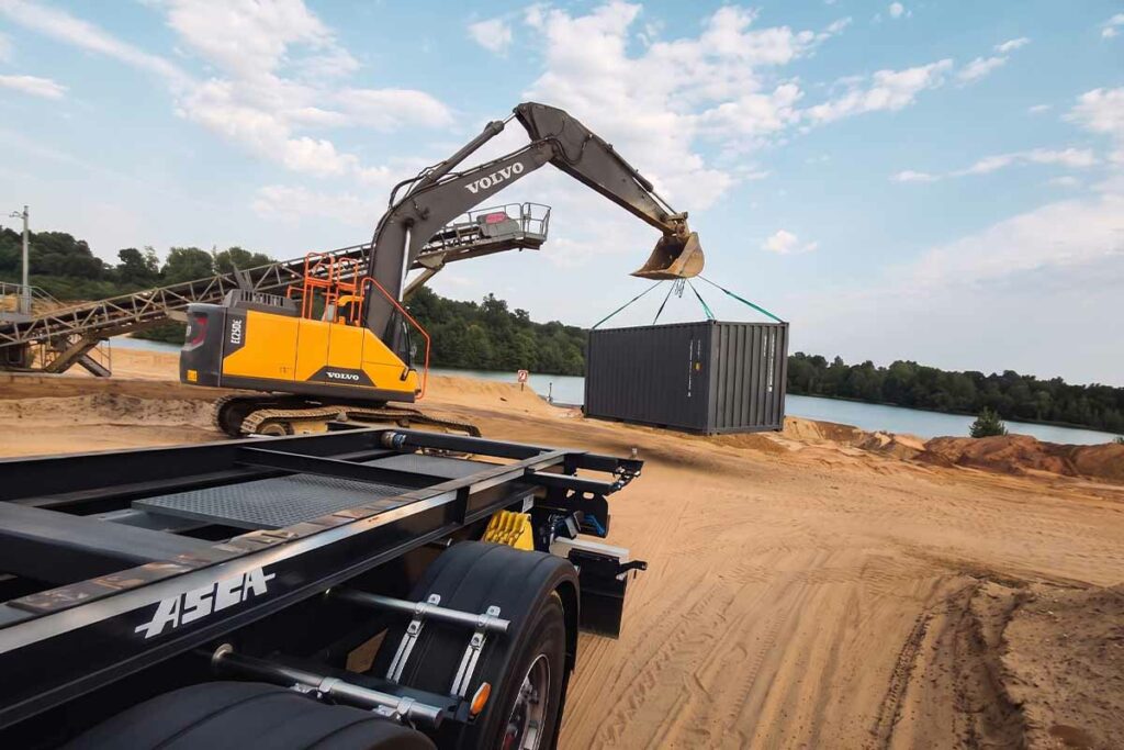 Container 20 pieds premier voyage transporté à la pelle au-dessus du sable, devant le plan d'eau d'une sablière