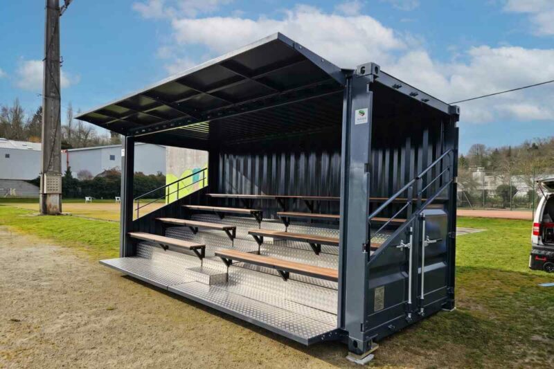 Tribune en container anthracite avec gradins couverts et auvent relevable, au bord du stade du Rugby Club de Nontron