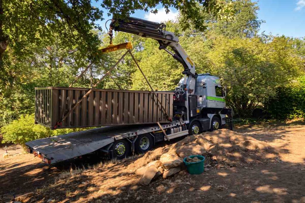 Camion-grue soulevant une piscine container 20 pieds sous les branches de chênes, lors d'une livraison en Dordogne