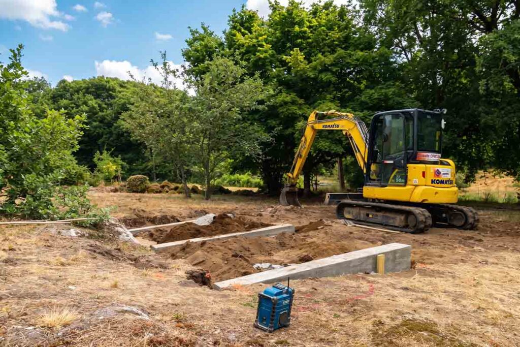 Trois longrines en béton coulées en parallèle, mini-pelle au fond, avant la pose d'une piscine container en Dordogne