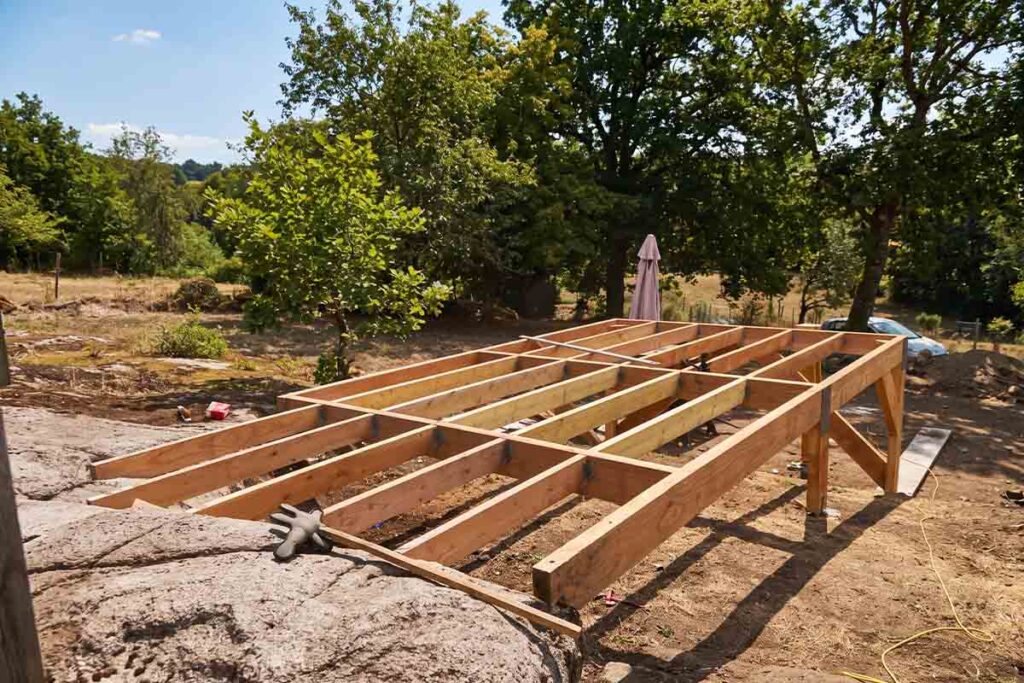 Ossature en bois d'une terrasse sur pilotis montée au-dessus de la roche, avant la pose d'une piscine container en Dordogne