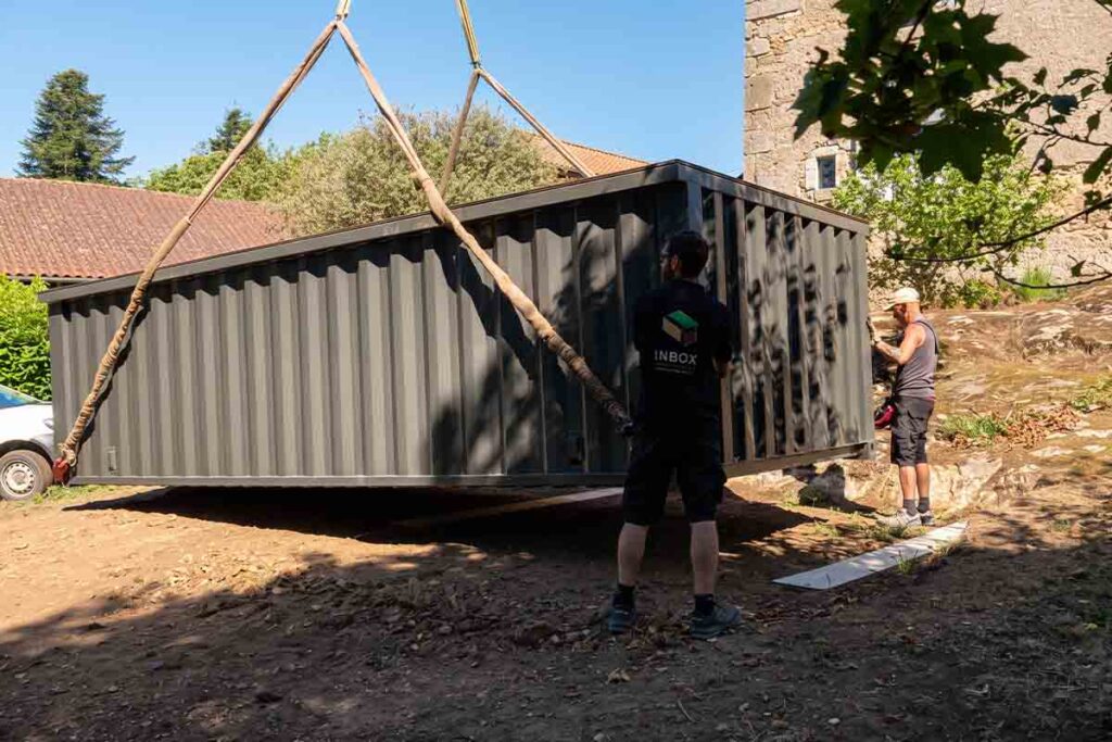 Piscine container 20 pieds suspendue à la grue, guidée à la main par une sangle avant sa pose, à Abjat-sur-Bandiat (24)